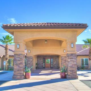 A sunny view of a building entrance with a covered walkway and palm trees.