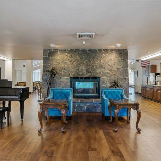 A spacious living room featuring a modern fireplace, blue armchairs, and a grand piano on a wooden floor.