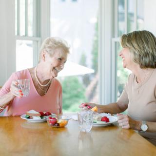 Two elderly women enjoying a lively conversation over a meal at the table.