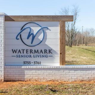 A sign for Watermark Senior Living located outdoors, featuring a brick base and wooden accents.