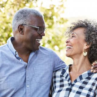 An elderly couple smiling at each other outdoors.