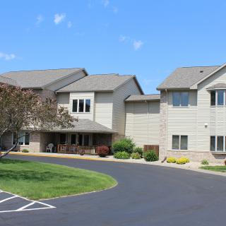 A modern residential building with a driveway and well-maintained landscaping on a sunny day.
