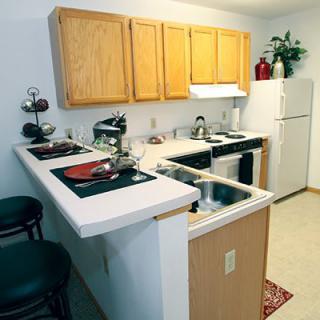 A compact kitchen with wooden cabinets, a white countertop, and bar seating.
