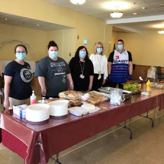 Volunteers prepare and serve food at a community event, ensuring safety with masks.