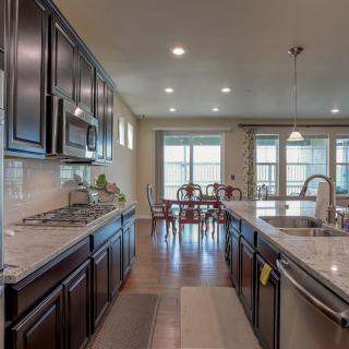 A modern kitchen with dark cabinets, a large island, and a dining area in an open-concept layout.