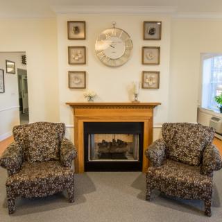 A cozy living room features a fireplace flanked by two patterned armchairs, with a decorative clock and wall art above.