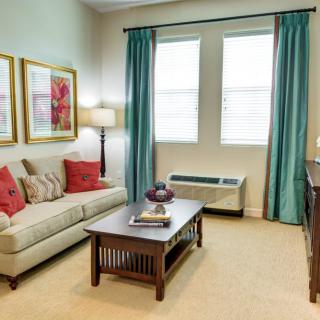 A cozy living room with a sofa, coffee table, and vibrant curtains. The space is decorated with wall art and colorful pillows.