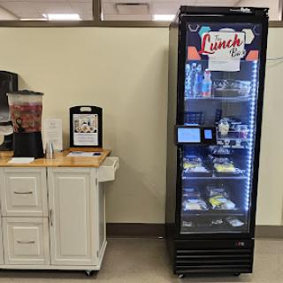 A modern vending machine offering various snacks and beverages, located in an office or break room setting.