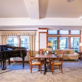 A cozy living room with a grand piano, table, chairs, and a sofa near large windows.