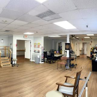 A spacious interior view of a rehabilitation center, featuring wooden floors and various office furniture.