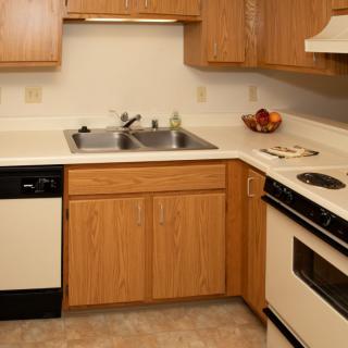A compact kitchen featuring wooden cabinets, a stainless steel sink, and standard appliances.