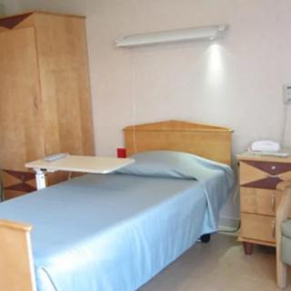 A simple hospital room with a bed, wardrobe, and bedside table.