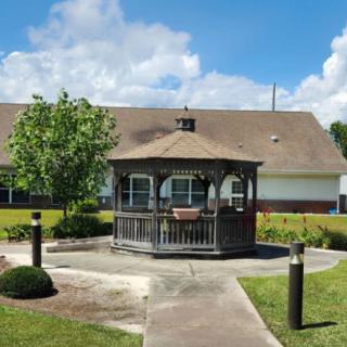 A wooden gazebo situated in a landscaped garden with a building in the background.