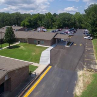 Aerial view of a building with a parking lot and surrounding greenery.