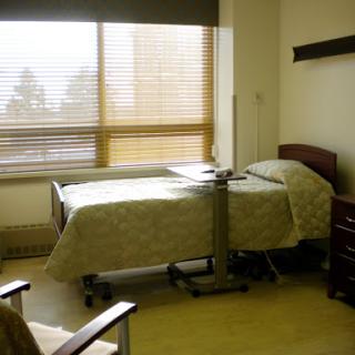 A well-lit hospital patient room featuring a bed, a chair, and a window with blinds.
