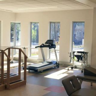 A well-lit gym room with exercise equipment including a treadmill and rehabilitation tools.