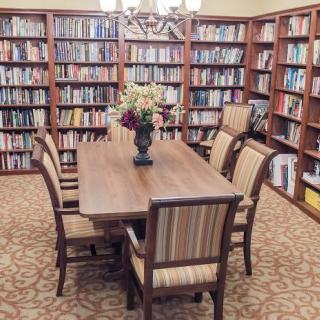 A quiet library reading room with a wooden table and chairs surrounded by bookshelves.
