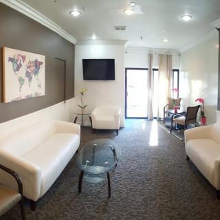 A modern waiting room featuring white sofas, a television, and decorative artwork on the walls.
