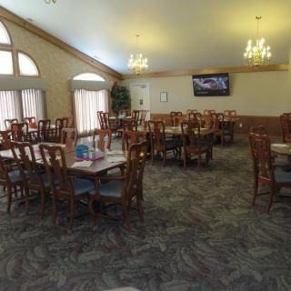 A spacious dining room with multiple tables and chairs, featuring a television and chandeliers.