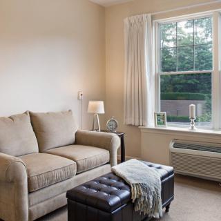 A cozy living room with a sofa, lamp, and window overlooking greenery.