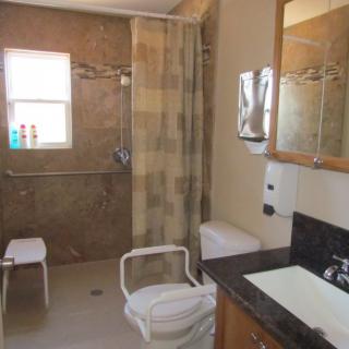 An accessible bathroom with a shower area equipped with grab bars, a shower chair, and a curtain.