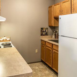 A small kitchen with wooden cabinets, a refrigerator, stove, and sink.