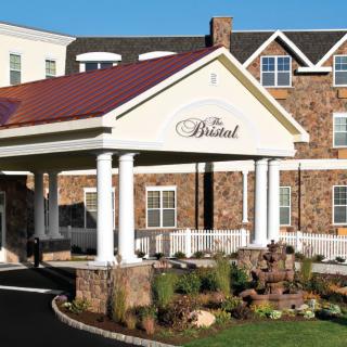 The entrance of a hotel with stone faade and landscaped surroundings.