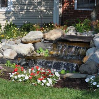 A small waterfall feature in a landscaped garden with colorful flowers and rocks.