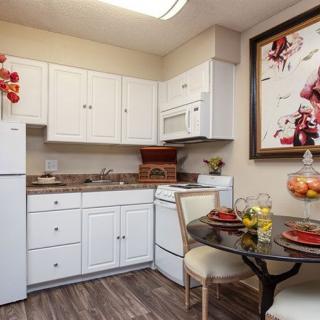 A cozy kitchen with white cabinets, a small dining table, and decorative artwork.