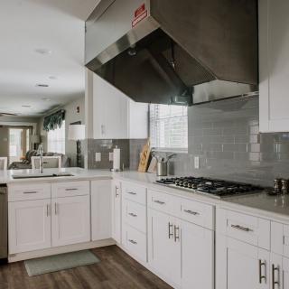 A modern kitchen with white cabinets, a stainless steel vent hood, and a gas stove.