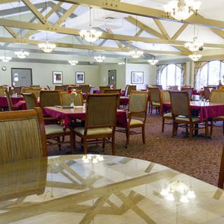 A spacious dining room with neatly arranged tables and chairs, featuring elegant lighting and wooden beams.