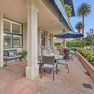 An outdoor patio area with tables and chairs under umbrellas, surrounded by lush greenery and palm trees.