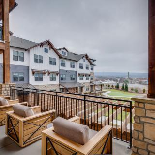 A cozy balcony with wooden chairs overlooking a residential building and landscape on a cloudy day.