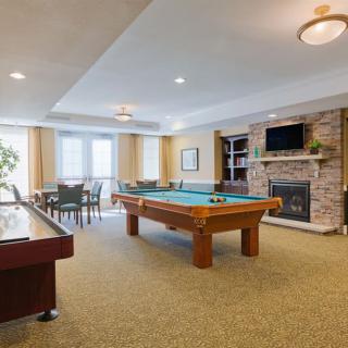 A cozy indoor game room featuring a pool table, shuffleboard, and a fireplace surrounded by a seating area.