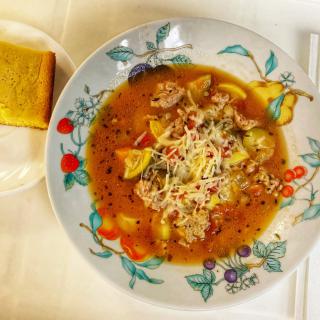 A hearty vegetable soup garnished with cheese, served with a slice of toasted bread.