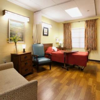 A well-furnished hospital room with a bed, armchair, and wooden flooring.