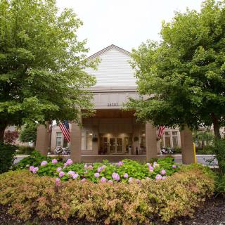 Front view of a building entrance with lush greenery and colorful flowers.