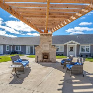A spacious patio with a wooden pergola covering a seating area centered around a stone fireplace.