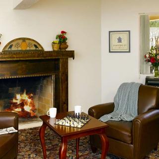 A cozy living room with a fireplace, two armchairs, and a chess game on the table.
