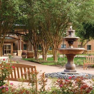 A serene garden featuring a central fountain surrounded by benches and vibrant flower beds.