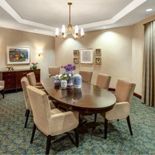 An elegant dining room featuring a large oval table surrounded by upholstered chairs, with tasteful artwork adorning the walls and a chandelier providing soft lighting.