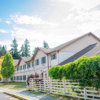 A suburban residential building with a white fence and surrounding trees on a sunny day.