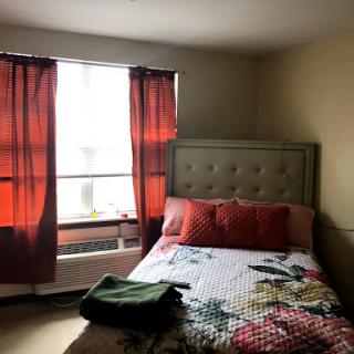 A cozy bedroom featuring a neatly made bed with floral bedding and warm red curtains.