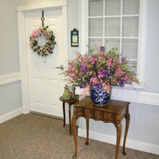 A small hallway with a wooden table adorned with a floral arrangement next to a door with a wreath.