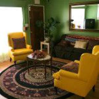 A cozy living room with vibrant yellow chairs, green walls, and a round decorative rug.