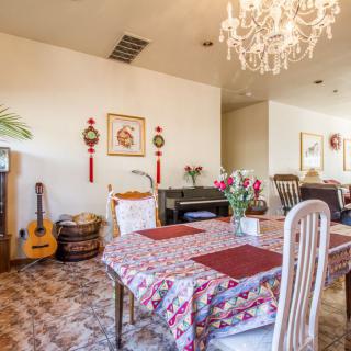 A cozy dining room featuring a chandelier, a floral tablecloth-covered table, and decorative elements including wall art and a guitar.