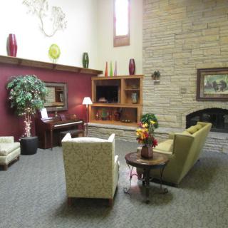 A cozy living room with a sofa, chairs, and a fireplace, featuring warm decor and indoor plants.