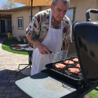 A man grilling burgers on a barbecue in the backyard on a sunny day.
