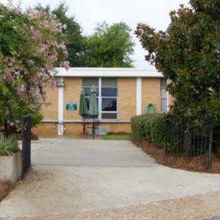 A small brick building with a driveway and surrounding greenery.