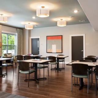 A modern dining room with neatly arranged tables and chairs, featuring contemporary lighting and artwork.